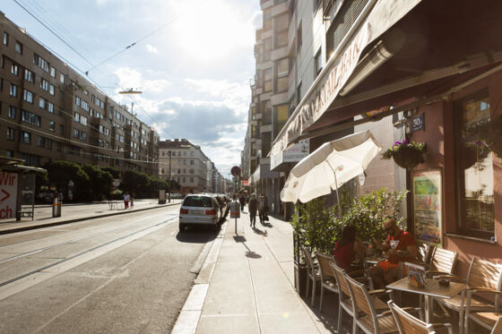 Straßenbahngleise, Straße mit Autos, Sonnenschirm Straße mit Café